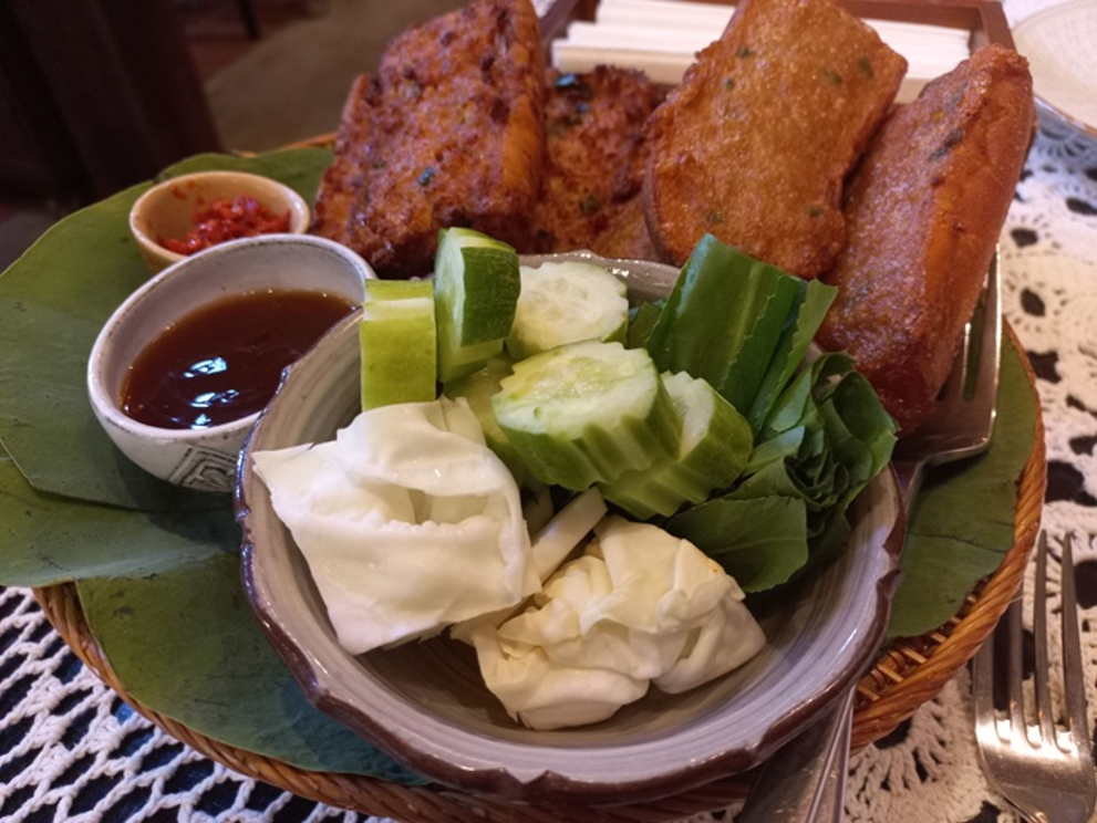 Crispy Cambodian fried bread topped with pork and fish cake, served with cucumber, cabbage, herbs and dipping sauces on a leaf lined tray at Maedy restaurant in Siem Reap.