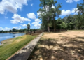 Stone terrace and shaded trees on the western edge of Sras Srang, with the large Angkor reservoir stretching out under blue sky and scattered clouds at midday.