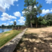 Stone terrace and shaded trees on the western edge of Sras Srang, with the large Angkor reservoir stretching out under blue sky and scattered clouds at midday.