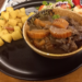 Close-up of boeuf-carottes with braised beef cheek and carrots, served in a rustic bowl alongside sautéed diced potatoes and fresh salad on a black plate at Graines de Piaf French bistrot in Siem Reap.