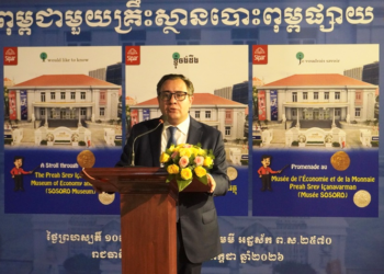 Blaise Kilian, co-directeur du musée SOSORO, prononce un discours de lancement devant un pupitre décoré de fleurs, avec en arrière-plan deux grands visuels du nouvel ouvrage illustré sur le Musée de l’Économie et de la Monnaie Preah Srey Içanavarman, en khmer, français et anglais