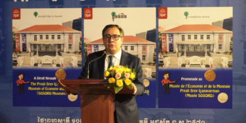 Blaise Kilian, co-directeur du musée SOSORO, prononce un discours de lancement devant un pupitre décoré de fleurs, avec en arrière-plan deux grands visuels du nouvel ouvrage illustré sur le Musée de l’Économie et de la Monnaie Preah Srey Içanavarman, en khmer, français et anglais