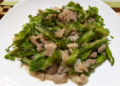 Close-up of Cambodian stir-fried winged beans with sliced pork on a white plate, glistening with light sauce and showing crisp green texture and home-style presentation.