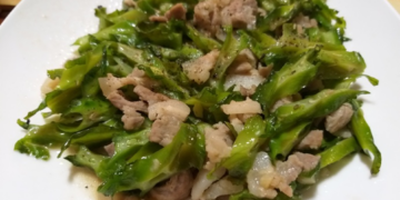 Close-up of Cambodian stir-fried winged beans with sliced pork on a white plate, glistening with light sauce and showing crisp green texture and home-style presentation.