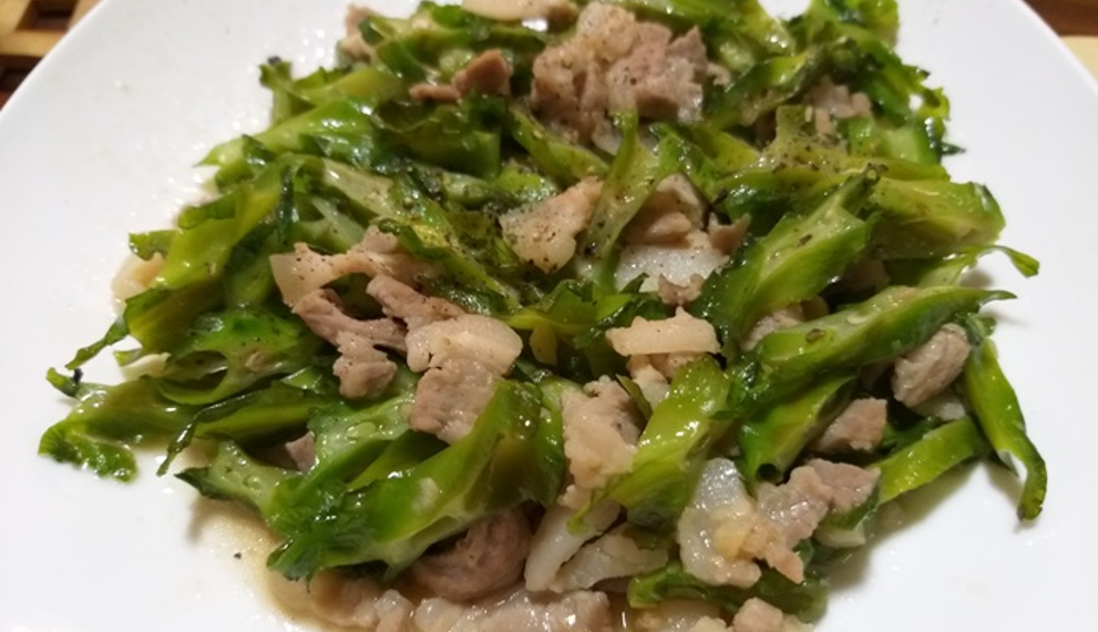 Close-up of Cambodian stir-fried winged beans with sliced pork on a white plate, glistening with light sauce and showing crisp green texture and home-style presentation.