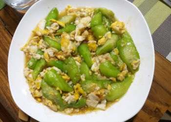 Plate of Cambodian luffa stir fried with scrambled eggs in light savory sauce on a wooden table, highlighting a simple Khmer home cooked meal.