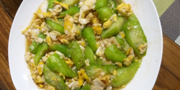 Plate of Cambodian luffa stir fried with scrambled eggs in light savory sauce on a wooden table, highlighting a simple Khmer home cooked meal.
