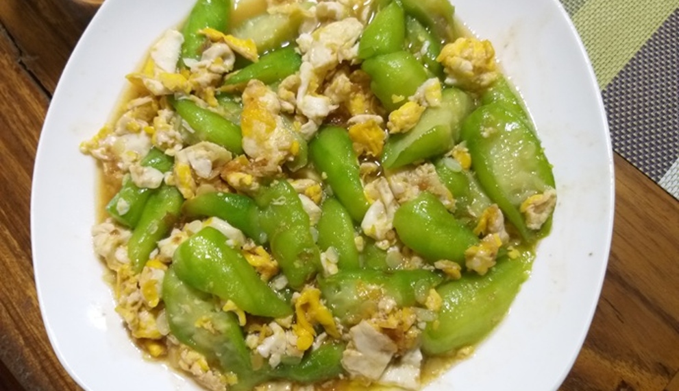 Plate of Cambodian luffa stir fried with scrambled eggs in light savory sauce on a wooden table, highlighting a simple Khmer home cooked meal.