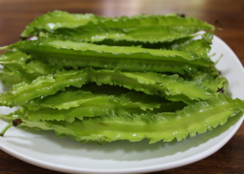 Close-up of several bright green winged bean pods on a white plate, showing their distinctive frilled edges and glossy surface.