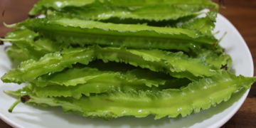 Close-up of several bright green winged bean pods on a white plate, showing their distinctive frilled edges and glossy surface.