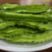 Close-up of several bright green winged bean pods on a white plate, showing their distinctive frilled edges and glossy surface.