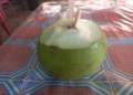 Fresh young green coconut with straw on patterned Khmer table on Phnom Chisor, Cambodia, highlighting affordable one dollar healthy coconut juice street drink.