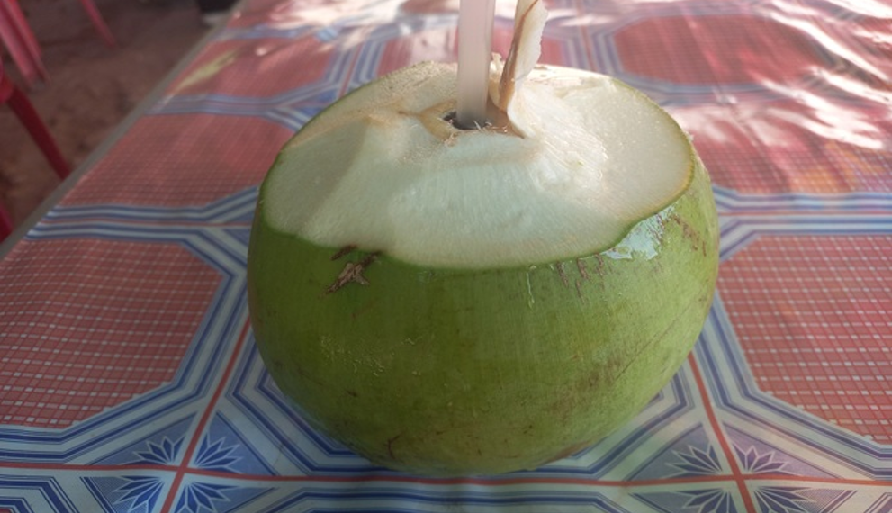 Fresh young green coconut with straw on patterned Khmer table on Phnom Chisor, Cambodia, highlighting affordable one dollar healthy coconut juice street drink.