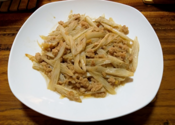Cambodian stir-fried lotus stem with ground pork on a white plate over a wooden table