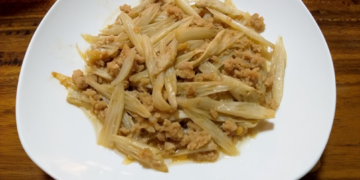 Cambodian stir-fried lotus stem with ground pork on a white plate over a wooden table