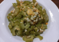 Close up of a white plate filled with Cambodian stir fried momordica bitter melon slices mixed with scrambled egg pieces, captured from above on a wooden table.