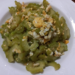 Close up of a white plate filled with Cambodian stir fried momordica bitter melon slices mixed with scrambled egg pieces, captured from above on a wooden table.