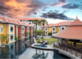 Aerial view of Memoire Palace Resort & Spa in Siem Reap showing bright villa-style buildings, central swimming pool, garden lawn and open-air bar at sunset.