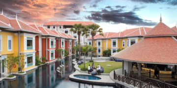 Aerial view of Memoire Palace Resort & Spa in Siem Reap showing bright villa-style buildings, central swimming pool, garden lawn and open-air bar at sunset.