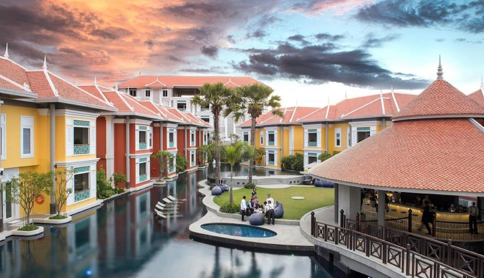 Aerial view of Memoire Palace Resort & Spa in Siem Reap showing bright villa-style buildings, central swimming pool, garden lawn and open-air bar at sunset.
