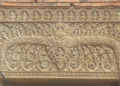 Sandstone lintel at Prasat Neang Khmao in Takeo, Cambodia, showing a central mythic face flanked by naga bodies, floral scrolls, and tiny seated figures above, carved in 10th century Khmer Koh Ker style on a brick temple façade.