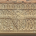Sandstone lintel at Prasat Neang Khmao in Takeo, Cambodia, showing a central mythic face flanked by naga bodies, floral scrolls, and tiny seated figures above, carved in 10th century Khmer Koh Ker style on a brick temple façade.