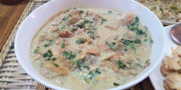Bowl of Cambodian kako tnaot soup with palm fruit, fish, and leafy greens in a creamy broth on a woven mat, traditional Khmer comfort food
