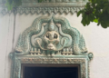 Decorative lintel of a modern pagoda near Phnom Chisor temple showing a seated Buddha framed by elaborate turquoise naga carvings and floral Khmer motifs above a doorway.