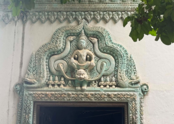 Decorative lintel of a modern pagoda near Phnom Chisor temple showing a seated Buddha framed by elaborate turquoise naga carvings and floral Khmer motifs above a doorway.