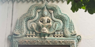 Decorative lintel of a modern pagoda near Phnom Chisor temple showing a seated Buddha framed by elaborate turquoise naga carvings and floral Khmer motifs above a doorway.
