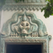 Decorative lintel of a modern pagoda near Phnom Chisor temple showing a seated Buddha framed by elaborate turquoise naga carvings and floral Khmer motifs above a doorway.