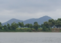 View of Phnom Neang Kangrei mountains reflected across a tranquil lake in Kampong Chhnang, Cambodia, under an overcast morning sky.