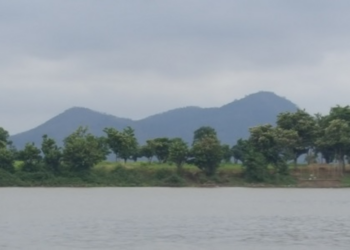 View of Phnom Neang Kangrei mountains reflected across a tranquil lake in Kampong Chhnang, Cambodia, under an overcast morning sky.
