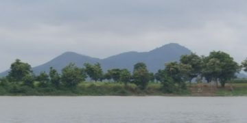 View of Phnom Neang Kangrei mountains reflected across a tranquil lake in Kampong Chhnang, Cambodia, under an overcast morning sky.