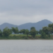 View of Phnom Neang Kangrei mountains reflected across a tranquil lake in Kampong Chhnang, Cambodia, under an overcast morning sky.