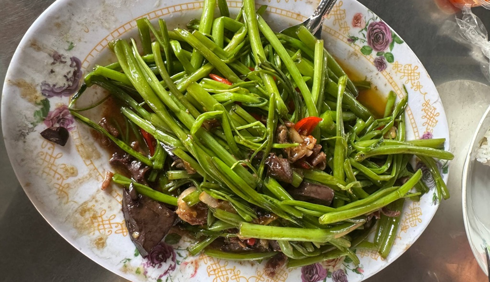 Stir-fried morning glory with chicken innards, chilies and garlic on a floral plate at a local eatery at Phnom Chisor temple in Takeo, Cambodia.