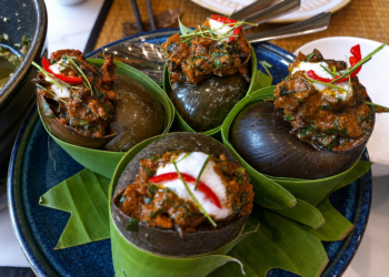 Snail amok served in large snail shells at Kraya Angkor Restaurant in Phnom Penh, featuring rich Cambodian coconut curry, fresh herbs, chili, and elegant presentation.