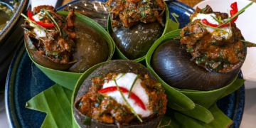 Snail amok served in large snail shells at Kraya Angkor Restaurant in Phnom Penh, featuring rich Cambodian coconut curry, fresh herbs, chili, and elegant presentation.