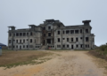Bokor Palace before restoration on Bokor Hill, Cambodia, showing the abandoned colonial-era building with its weathered façade under an overcast sky.