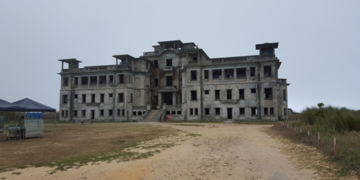 Bokor Palace before restoration on Bokor Hill, Cambodia, showing the abandoned colonial-era building with its weathered façade under an overcast sky.