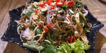 Cambodian beef innards salad with herbs, vegetables, peanuts, and red chilies served on a black plate in Kampong Thom.