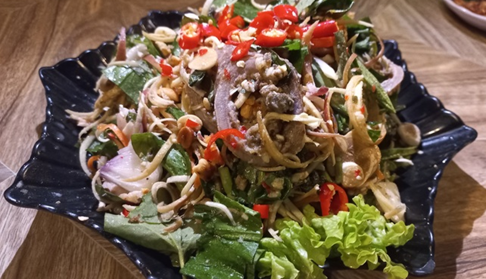 Cambodian beef innards salad with herbs, vegetables, peanuts, and red chilies served on a black plate in Kampong Thom.