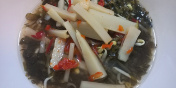 A bowl of Cambodian pickled bamboo shoots with African cabbage, chilies, bean sprouts, and herbs in a light brine.