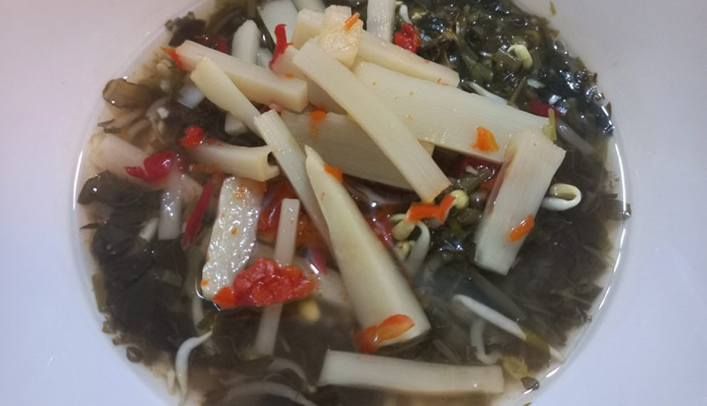 A bowl of Cambodian pickled bamboo shoots with African cabbage, chilies, bean sprouts, and herbs in a light brine.