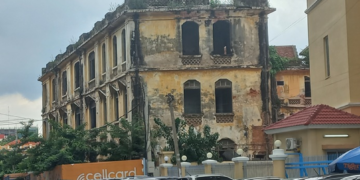 Old colonial-era commissariat building near Wat Phnom in Phnom Penh, Cambodia, with weathered yellow walls overlooking a busy street.