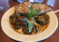 A plate of Cambodian snail curry with creamy coconut sauce, fresh basil, and grilled bread served at Bai Sor Restaurant in Phnom Penh.