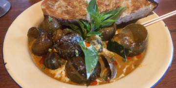 A plate of Cambodian snail curry with creamy coconut sauce, fresh basil, and grilled bread served at Bai Sor Restaurant in Phnom Penh.