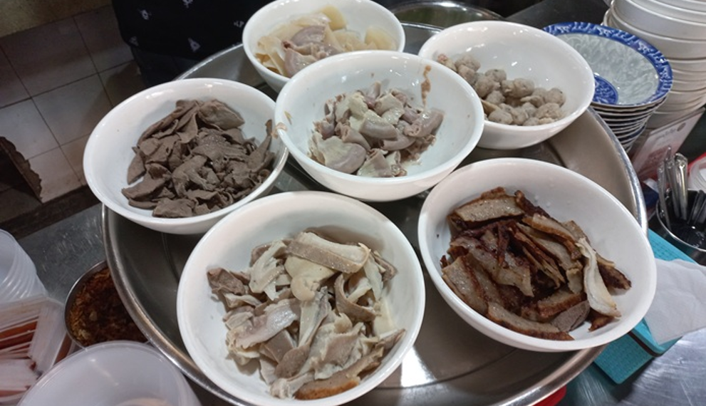 Bowls of meat, pork offal, meatballs, and other ingredients for បបរសាមចូក at Central Market in Phnom Penh, Cambodia