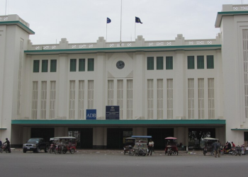 Historic Phnom Penh Railway Station with its distinctive Art Deco architecture, central clock, green accents, and busy street scene.