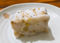 Slice of នំចេកខ្ទិះដូង, Cambodian banana cake with coconut cream and sesame seeds on a white plate.